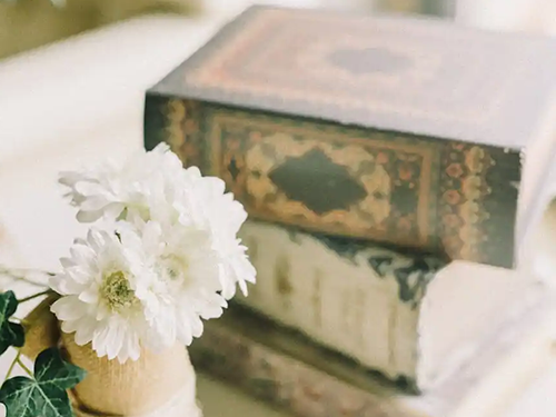 wooden vase with flowers in front of three stacked books